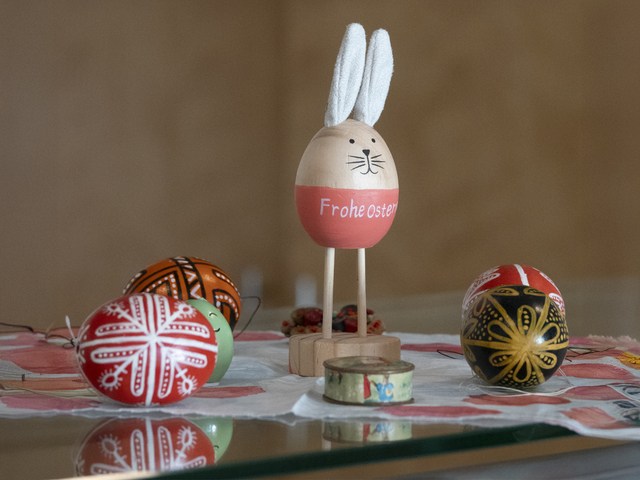 Ein Ei aus Holz, geschmückt als Osterhase, mit der Aufschrift 'Frohe Ostern' - umgeben von weiteren Ostereiern